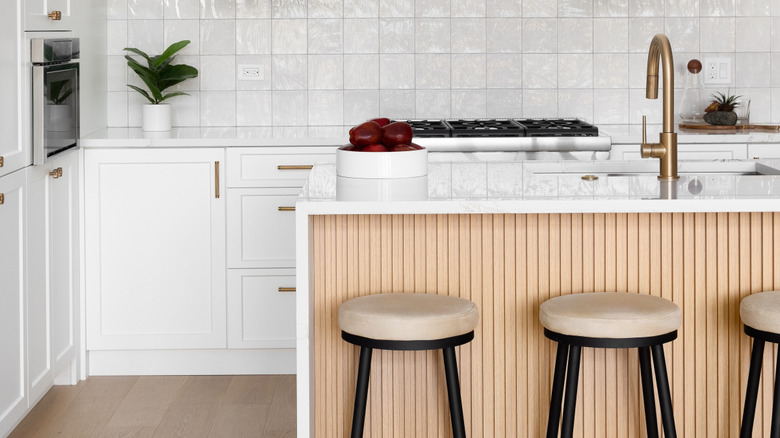 A white kitchen with a waterfall island, decked with wood paneling on the front