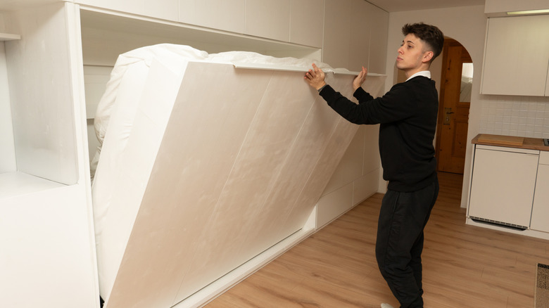 man raising Murphy bed into wall