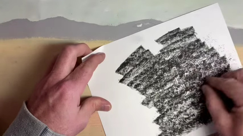 A pair of hands rubbing some charcoal onto a piece of paper
