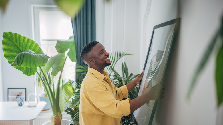 A man smiles as he hangs a piece of wall art in his home