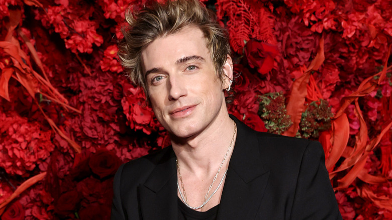 Jeremiah Brent wearing all black and posing at an upscale event, standing in front of a floral wall with rich red colors.