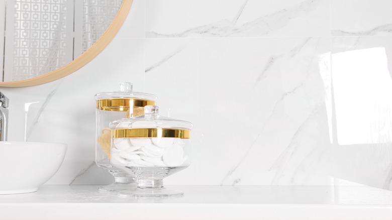 Bathroom essentials organized in two glass jars on a white marble countertop