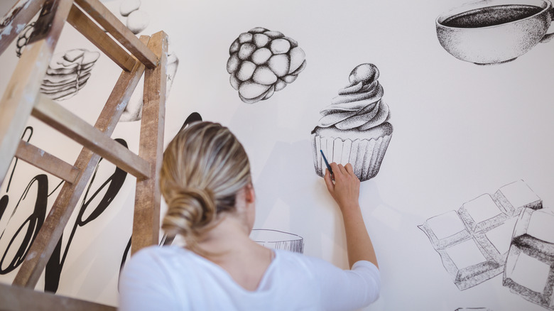 woman painting black and white images of food on interior wall