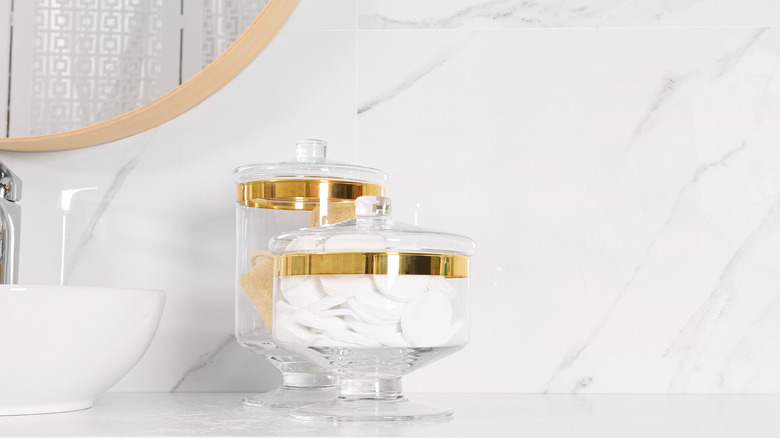Bathroom essentials organized in two glass jars on a white marble countertop