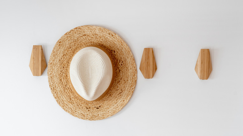 A set of wooden hooks on the wall with a sunhat.