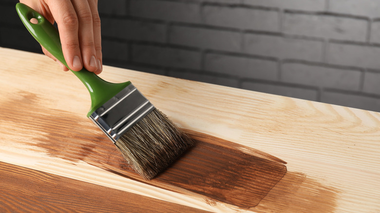 A hand staining a piece of wood with a brush