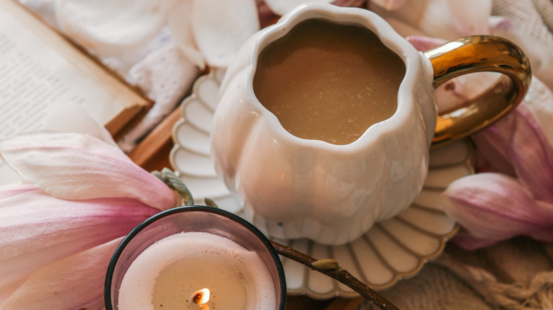 A tea cup on a scalloped saucer next to a book, candle, and real flower.