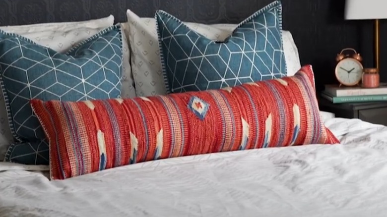 A beautiful long pillow made from a colorful rug and displayed on a bed in front of other cushions