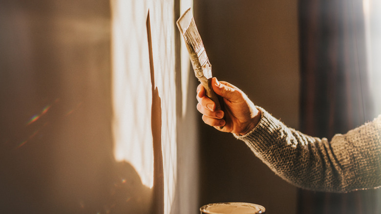 Person's hand painting wall with paintbrush