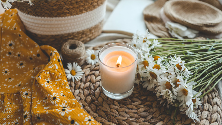 Candle centered on a coaster, daisies, and mustard yellow fabric
