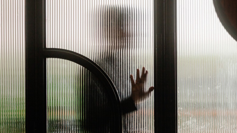 Figures silhouetted behind reeded glass, hands pressed against the surface.
