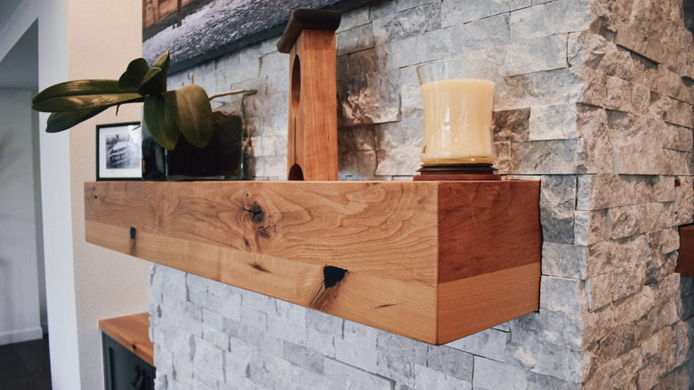 A wood mantel on a stone fireplace.