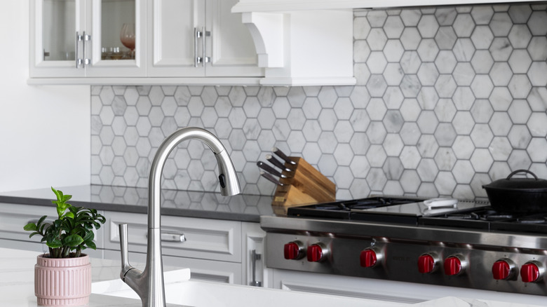 A kitchen with hexagonal tile backsplash and white cabinets