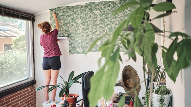 A person puts up botanical-themed wallpaper.