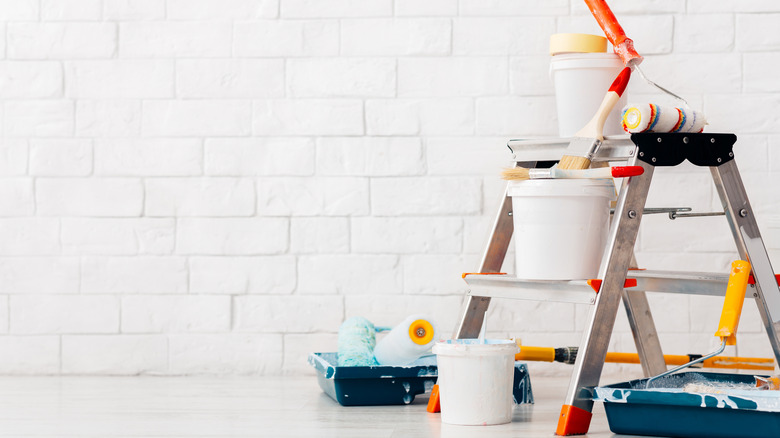 Brick wall painted white with paint supplies and ladder