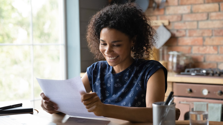 A smiling woman reads a letter happily.
