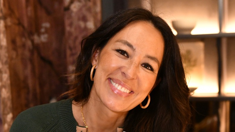 Joanna Gaines smiles at the camera with her head tilted.