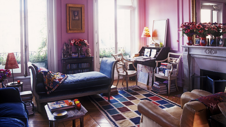 A brightly colored maximalist living room filled with stacks of books and vases of fresh flowers