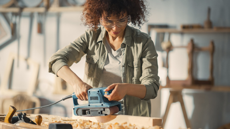 A woman sanding wood, wearing protective eyewear