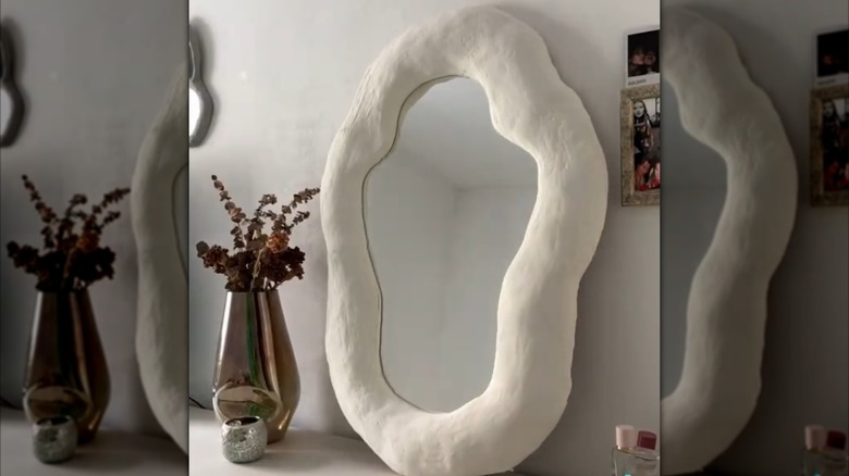 Unpainted squiggly clay mirror on dresser beside plant
