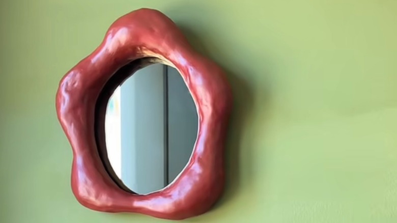 Red hand-sculpted clay squiggly mirror on green wall