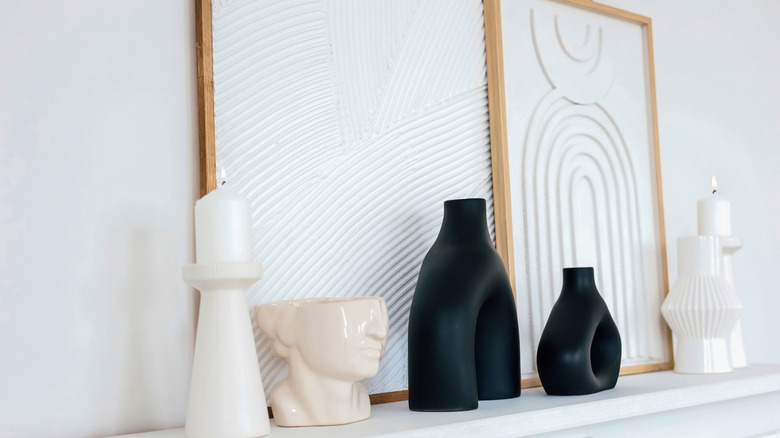 Framed artwork, candle, and accessories sitting on simple white mantel