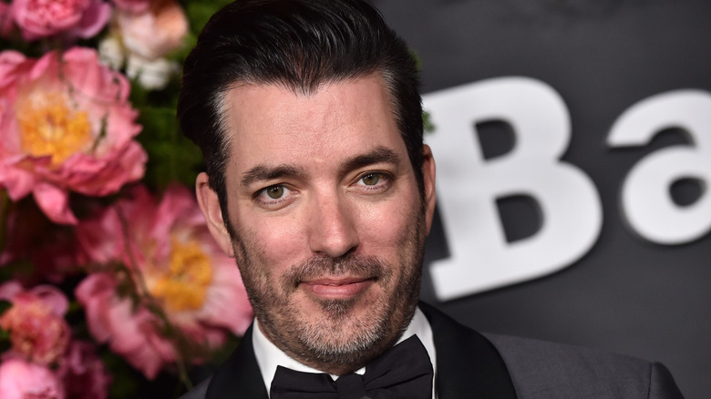 Jonathan Scott posing in a tuxedo in front of a spray of pink and yellow flowers.