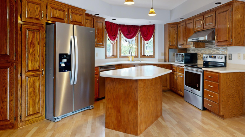 A kitchen with dark wood cabinets, white counters, and red curtains