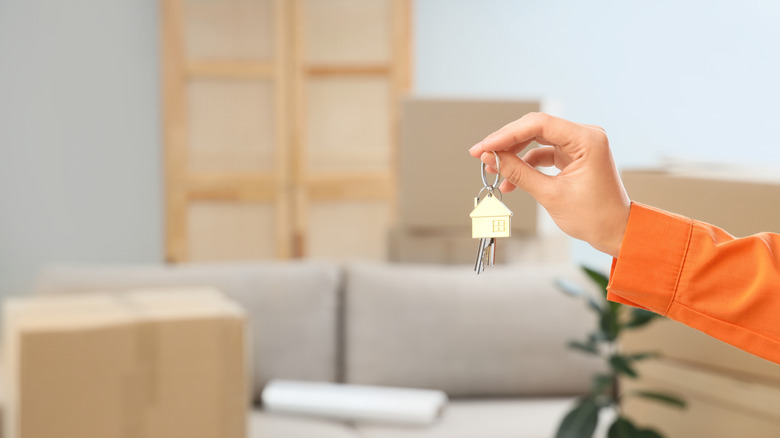 A person holding up a set of keys in an apartment with moving boxes in the background