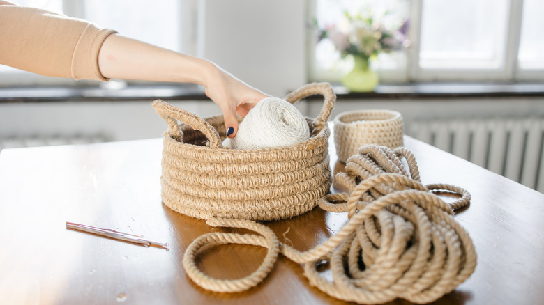 Person placing an item into a homemade jute basket, with leftover jute rope on the table