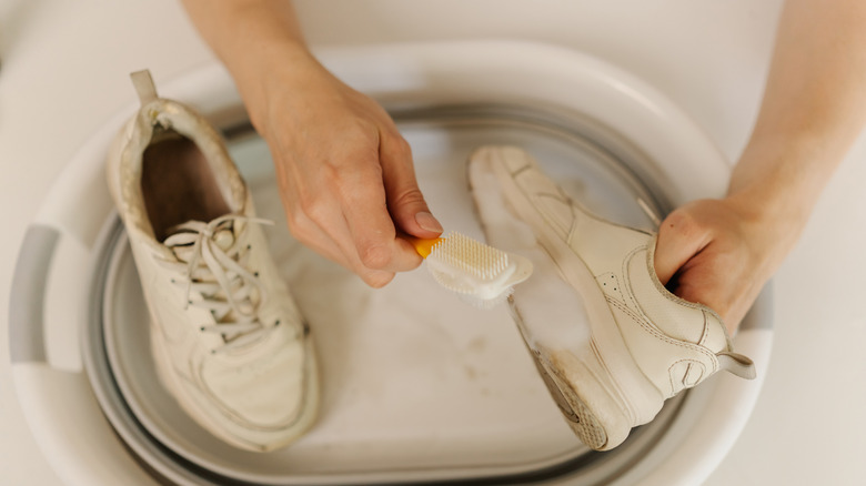 A hand scrubbing dirty white shoes with a brush
