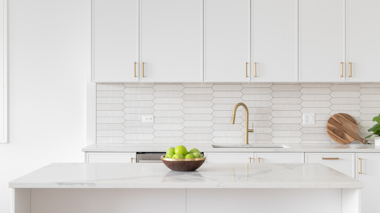 all-white kitchen with gold sink faucet and bowl of apples on kitchen island