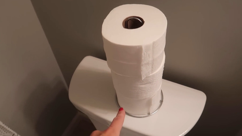 Toilet paper rolls stacked using a paper towel holder on top of a toilet tank.