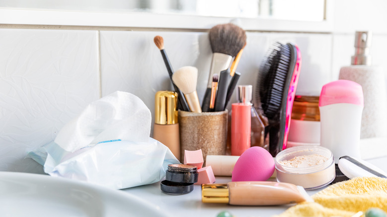 Cluttered bathroom countertop covered in makeup and toiletries