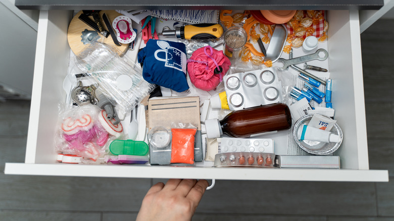 Hand pulling a drawer open that is messy and unorganized with all sorts of mismatched items.