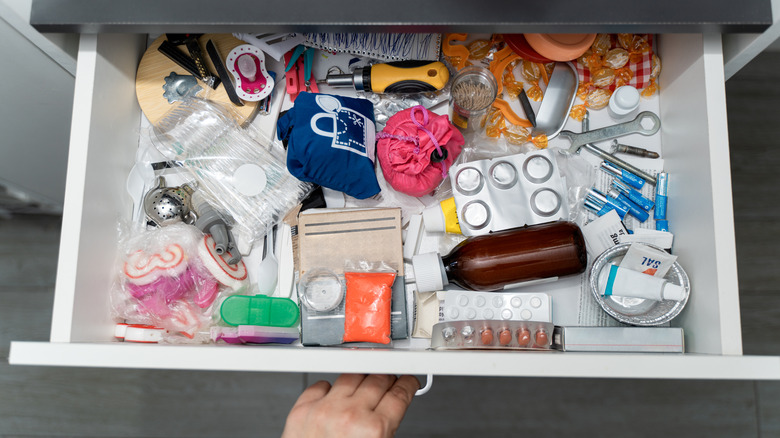 A person opens a messy drawer with items scattered randomly