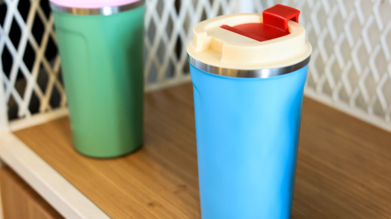 Two colorful reusable coffee tumblers on a metal wire shelf