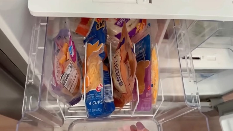 A white wire Dollar Tree dish rack placed in the drawer of a refrigerator holds bags of cheese