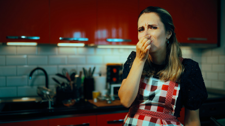 Woman standing in the kitchen covering her nose because it smells bad