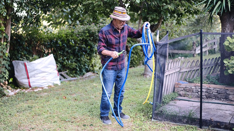 A gardener untangling a blue hose to water the garden