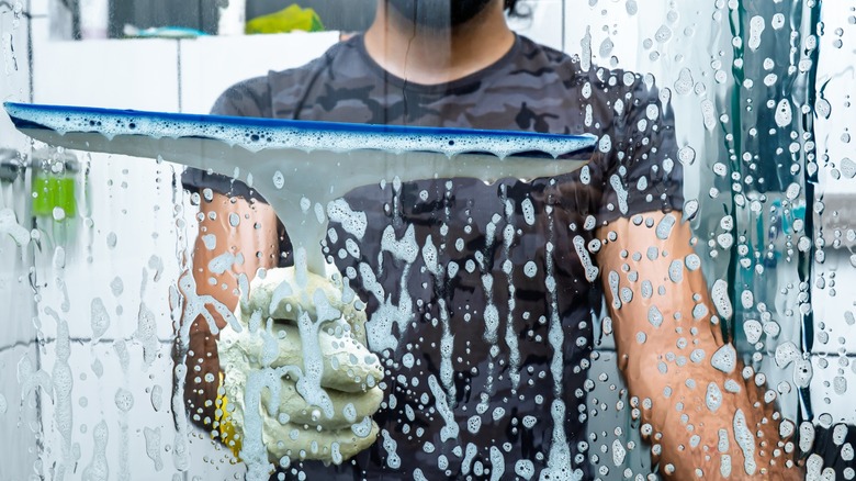 Person using a squeegee to remove cleaner and water from glass shower door