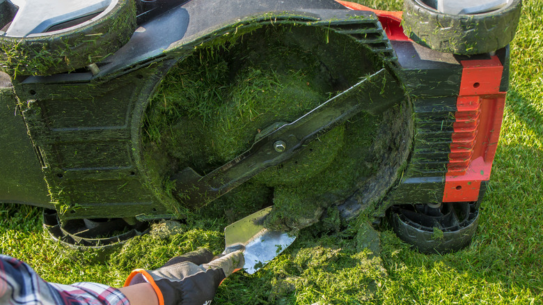 A man using a trowel to remove grass from a lawn mower deck