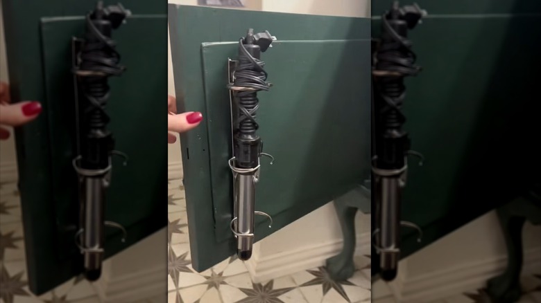Hair curling iron hung in a metal binder ring mounted to the inside of a green cabinet