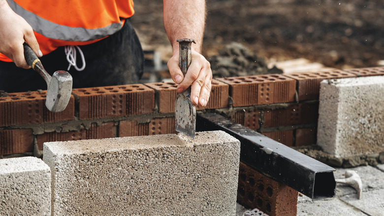 A person cutting a concrete block with a hammer and chisel