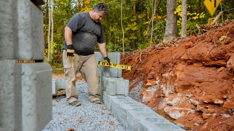 A person using a level while building a block retaining wall