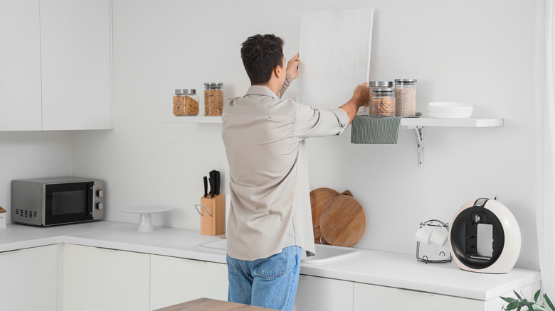 A man organizing kitchen items and decor on a wall shelf
