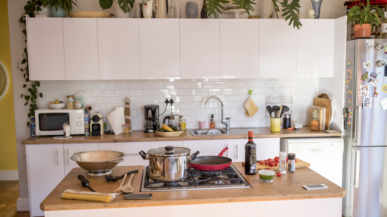 A kitchen is cluttered with pots, pans, bottles, and the makings of a meal.