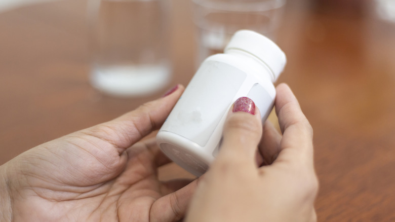 A hand with painted nails holding a prescription bottle