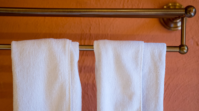 Close up photo of two white towels hanging on a towel bar on an orange background
