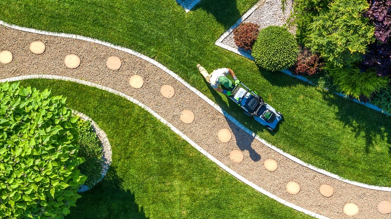Aerial view of a person mowing a lawn along gravel pathway and landscaped flower beds